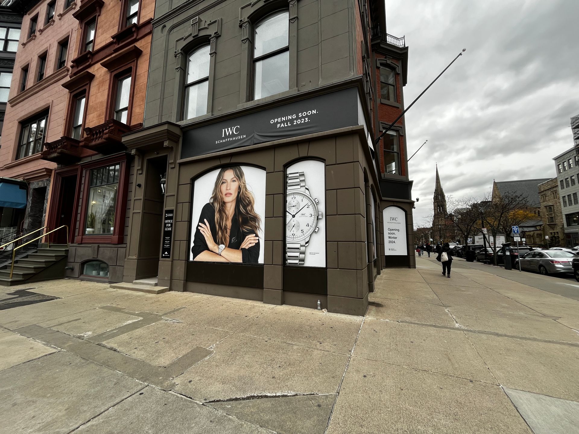 Corner storefront on a city street with fashion posters and brick buildings under a cloudy sky.