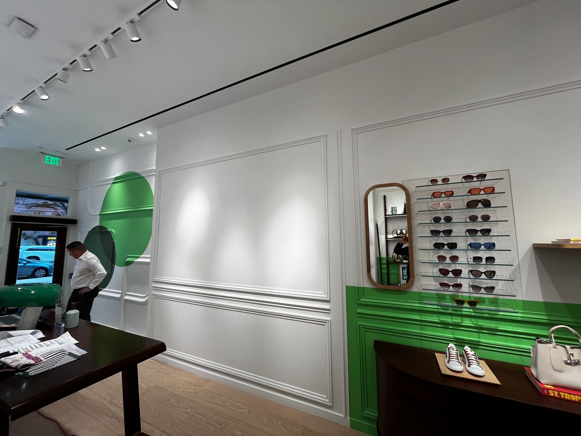 Bright retail boutique interior with green accents, wall-mounted shoe displays, and a person near the counter