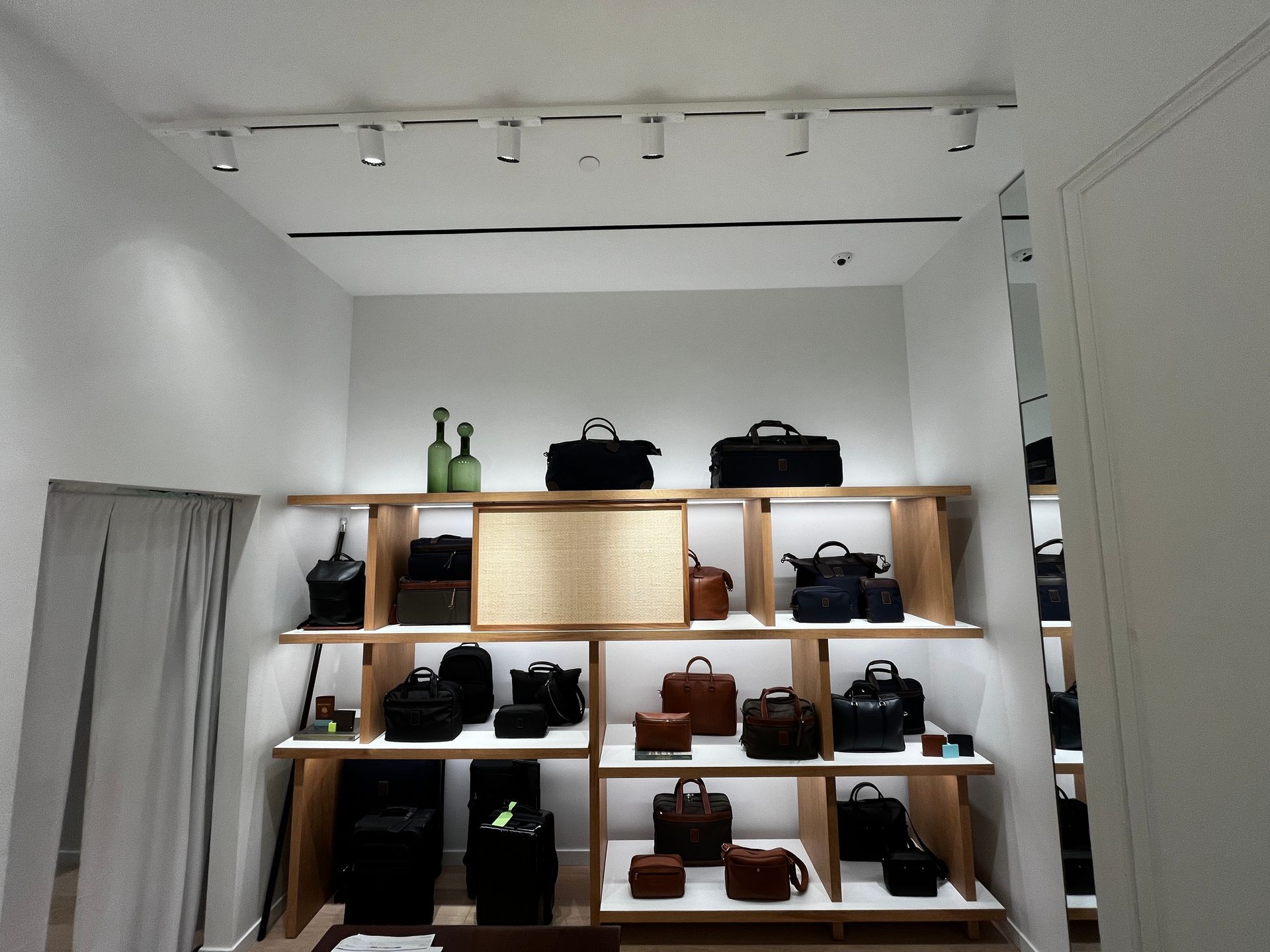 Wall display of handbags and boots in a minimalist boutique with wood shelves and white walls