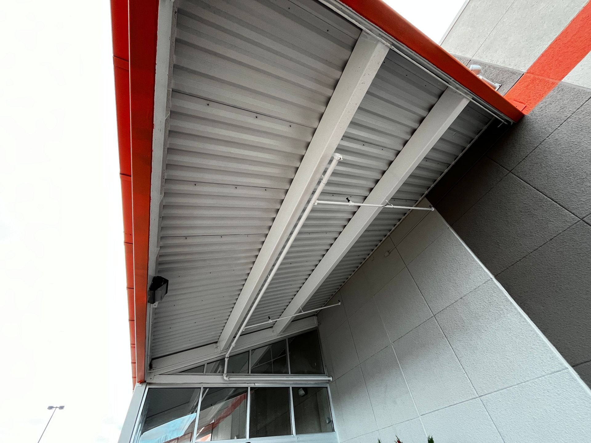 Underside of a modern building awning with red trim and gray panels at an angle
