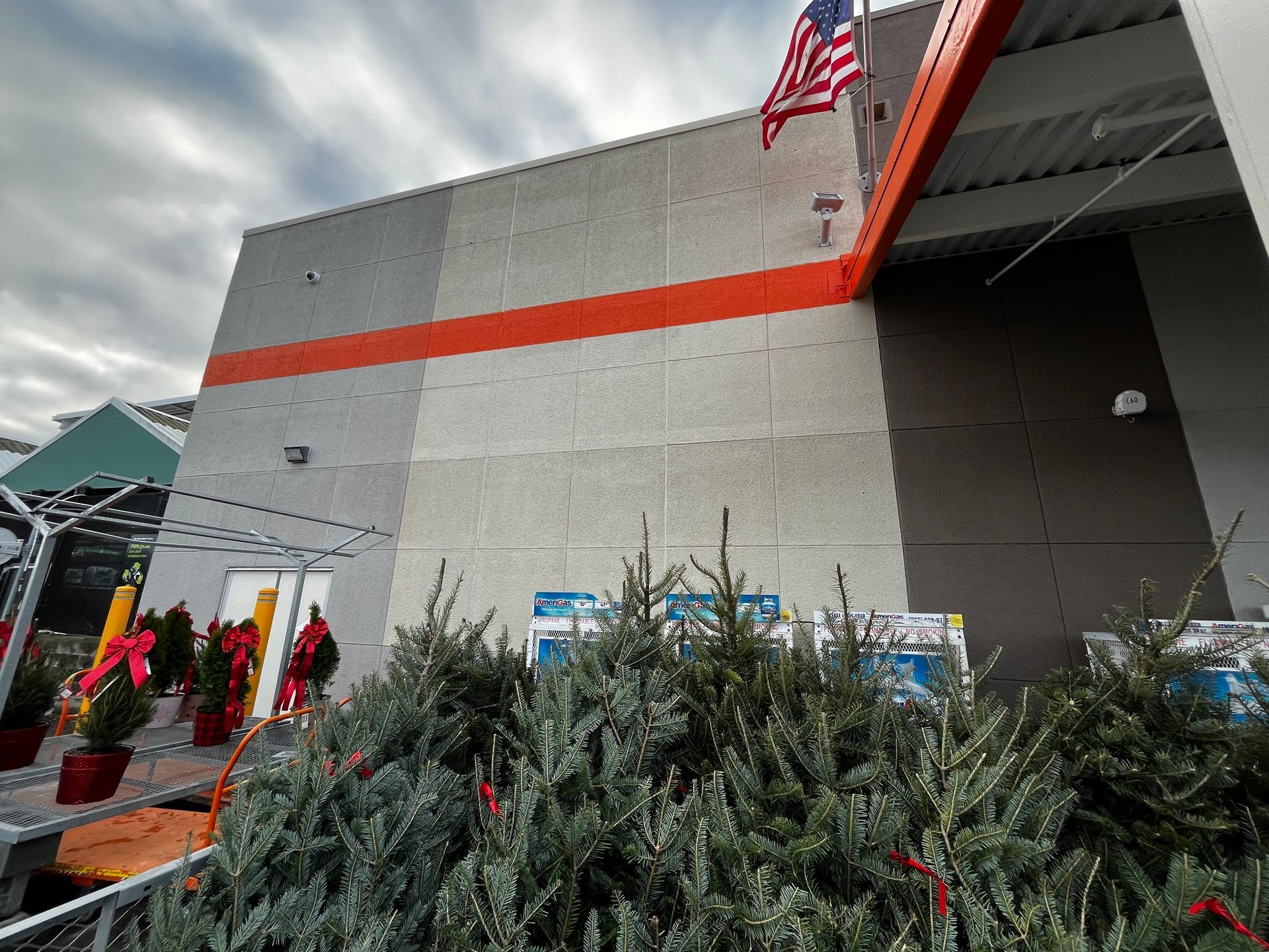 Outdoor store entrance with holiday trees, red decorations, and an American flag on the building.