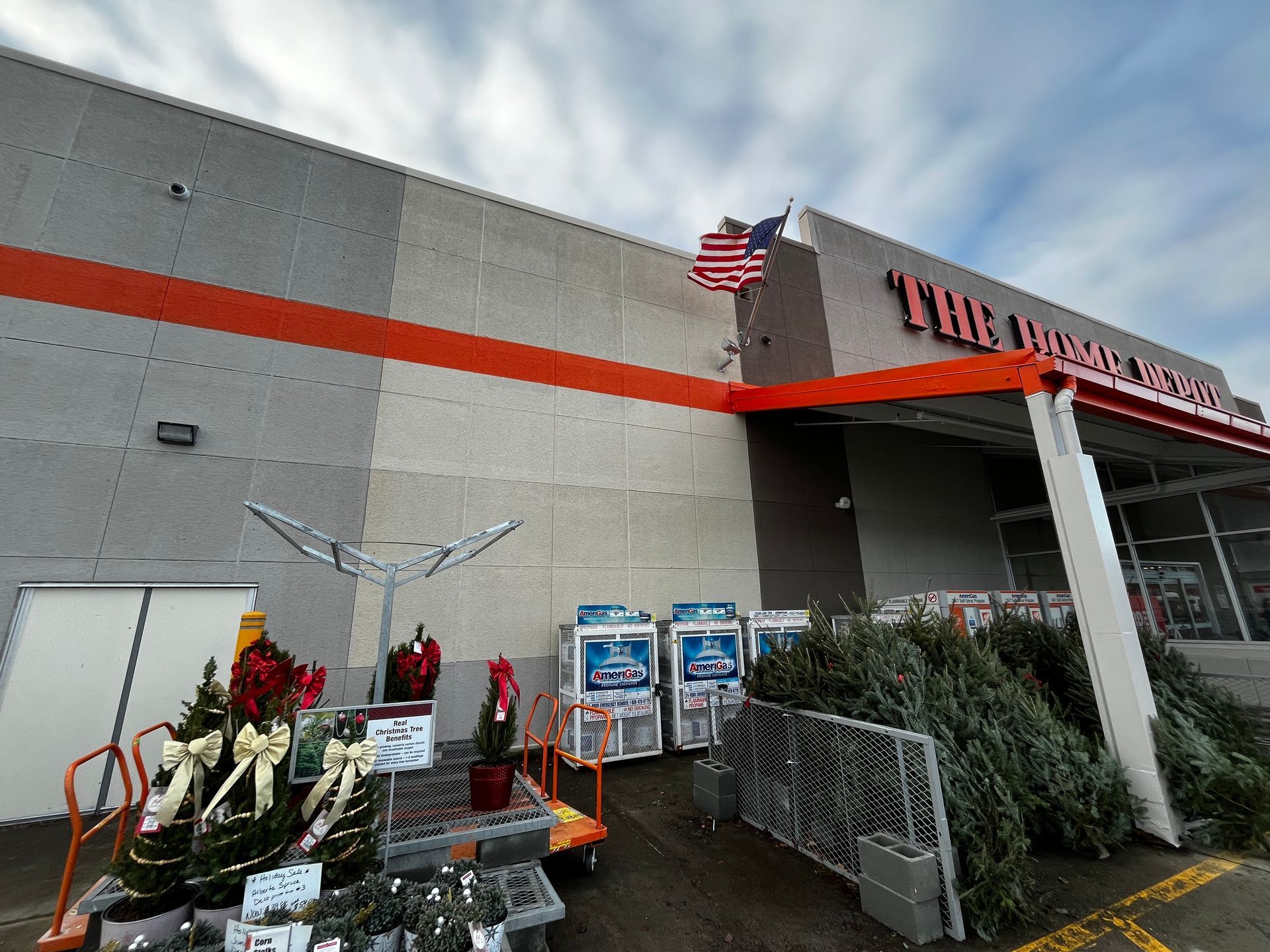 Home improvement store entrance with flowers, flags, carts, and plant displays outside.