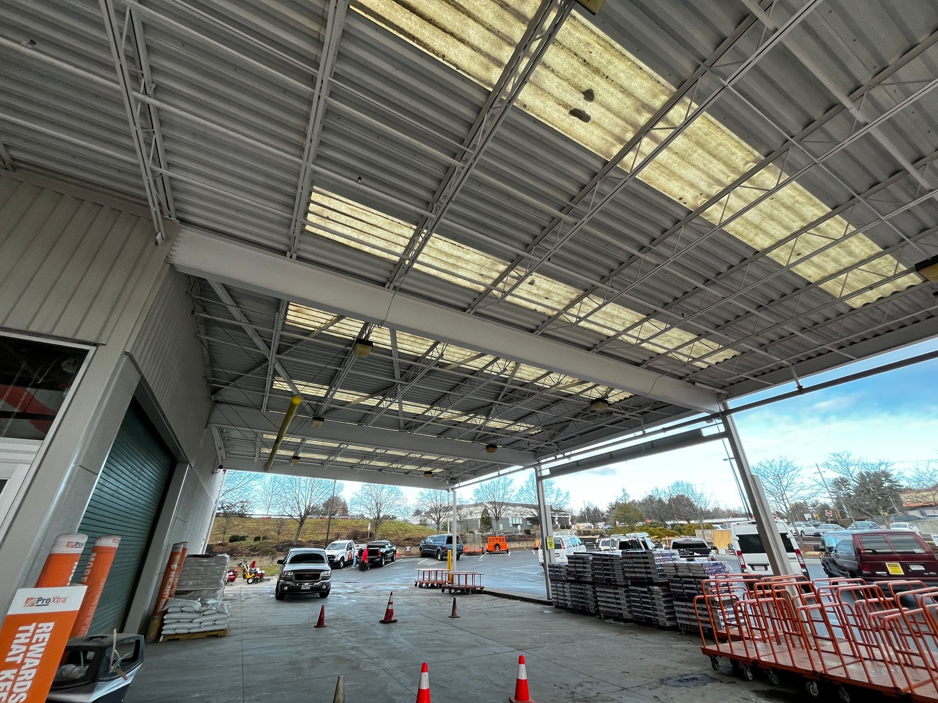 Covered outdoor store entrance with parked cars, shopping carts, and orange safety cones under a metal canopy