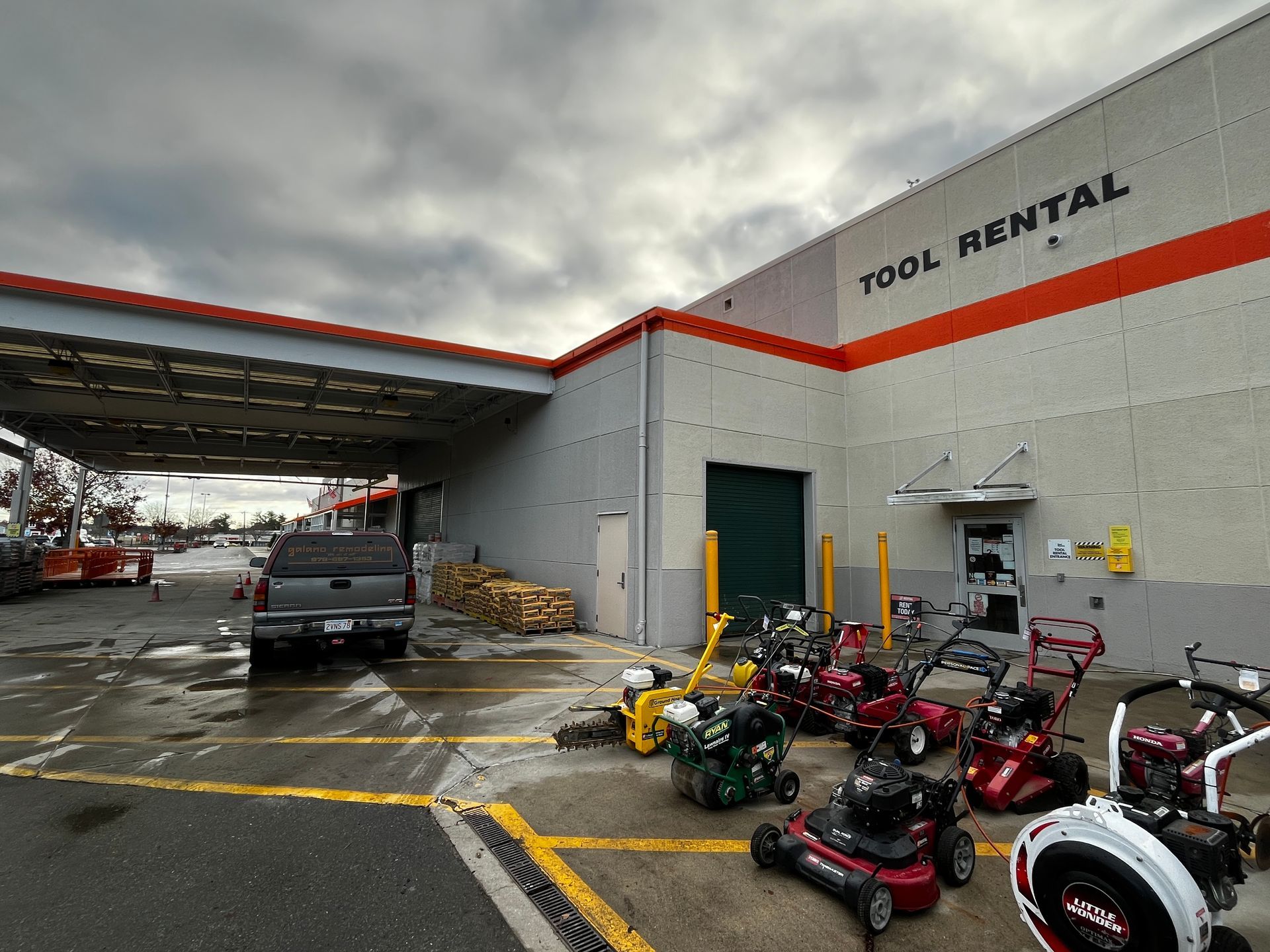 Tool rental store exterior with rows of lawn equipment and a wet parking lot