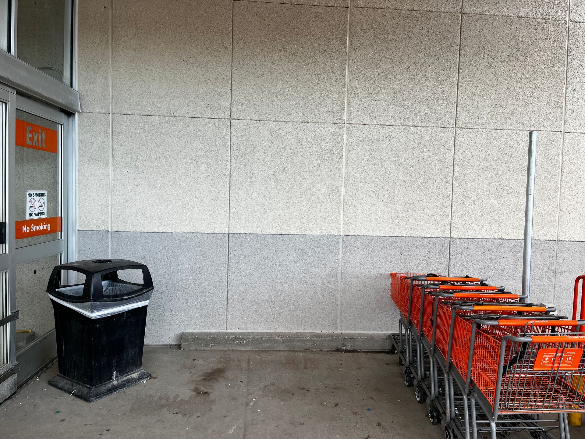 Store entrance with a trash can and a row of orange shopping carts against a tiled wall.