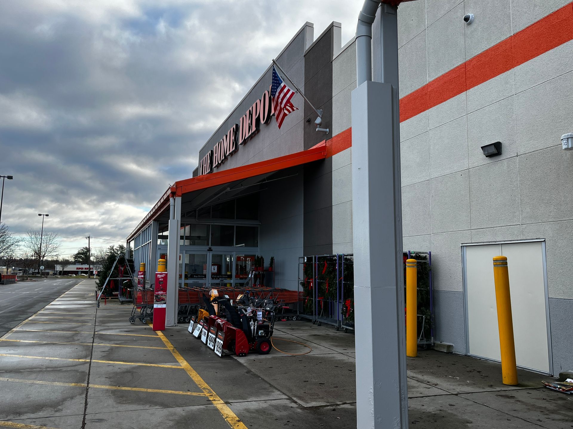 Home improvement store entrance with orange awning, shopping carts, and parked bikes under cloudy sky