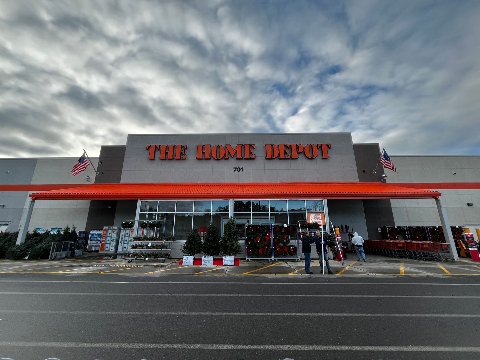 The Home Depot storefront with orange awning under a cloudy sky, carts and shoppers outside