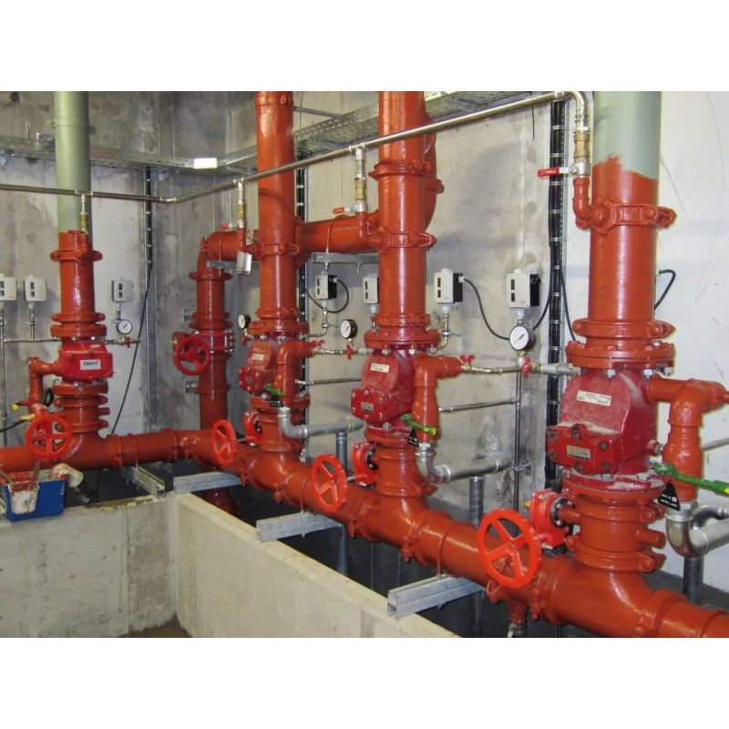 Red industrial pipes and valves in a mechanical room, with gauges and flanges on concrete floors.