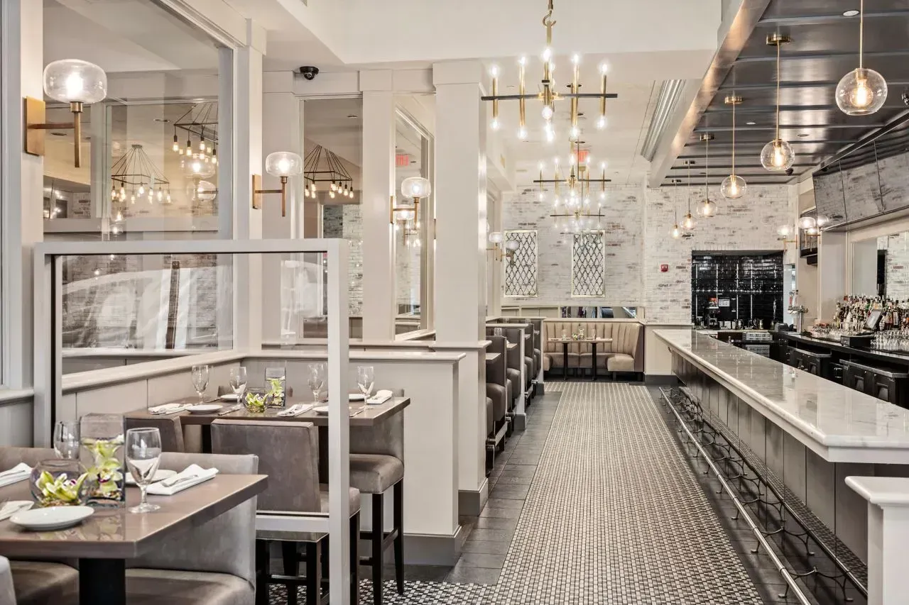 Elegant restaurant interior with white booths, marble counters, and patterned black-and-white tile flooring