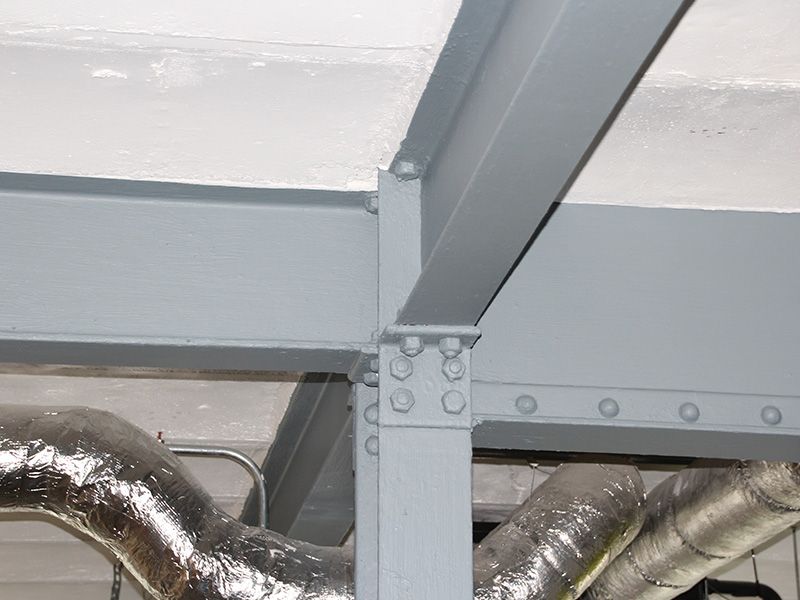 Gray metal beams and shiny insulated ductwork in an industrial ceiling area.