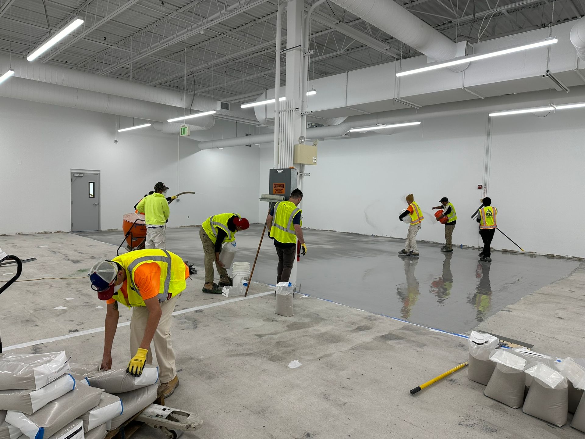 Workers in yellow vests leveling wet concrete in a large indoor construction site