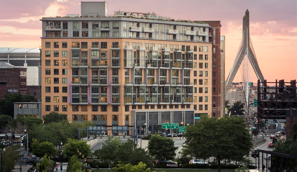 Modern apartment building at sunset with a city skyline and bridge in the background