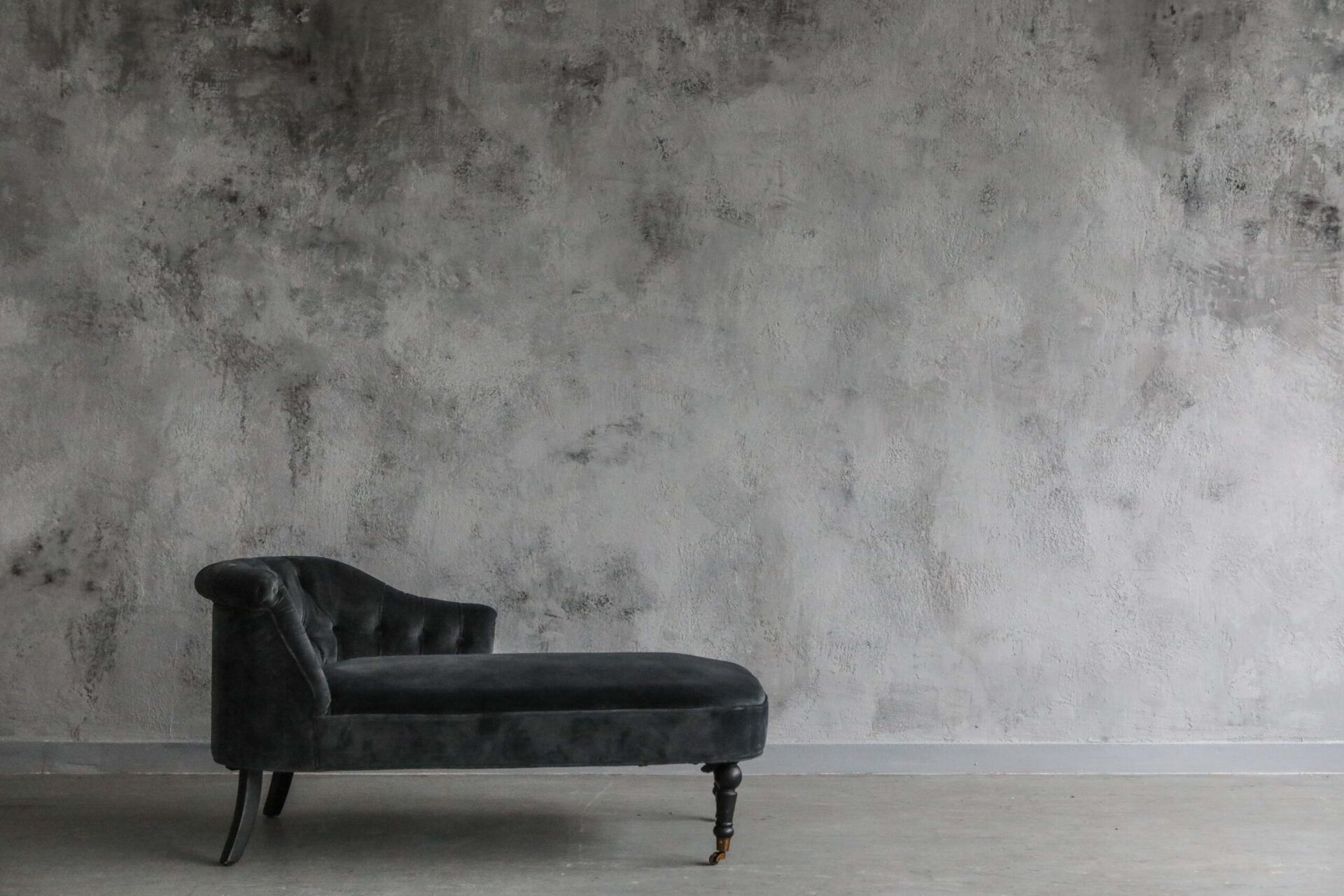 Black chaise lounge against a gray textured wall in a minimalist room