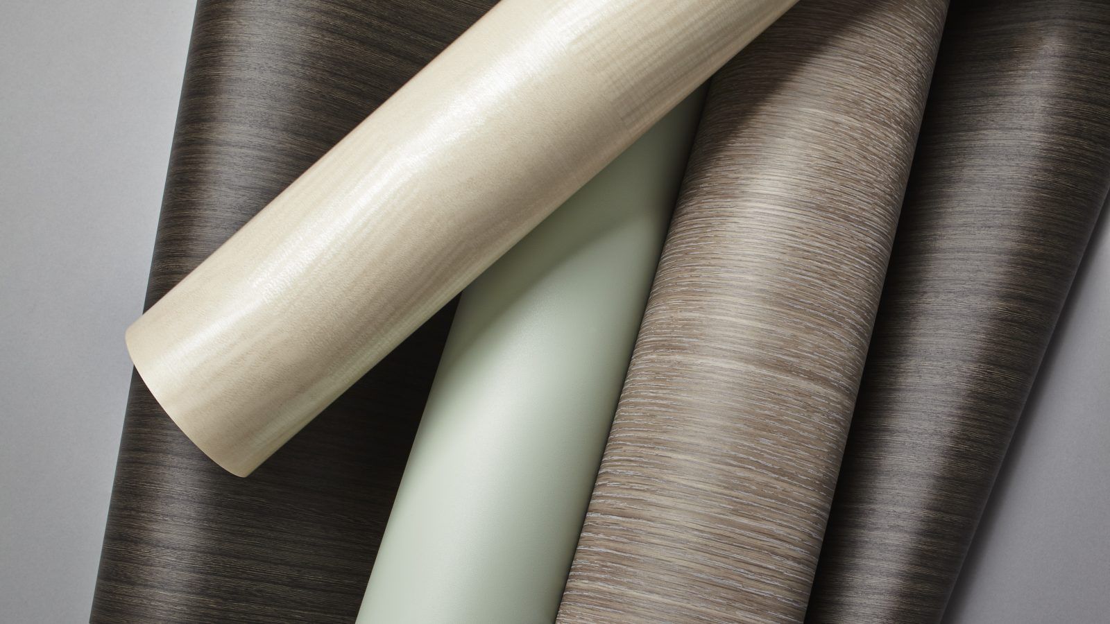 Rolled wallpaper samples in beige, mint, taupe, and gray arranged diagonally