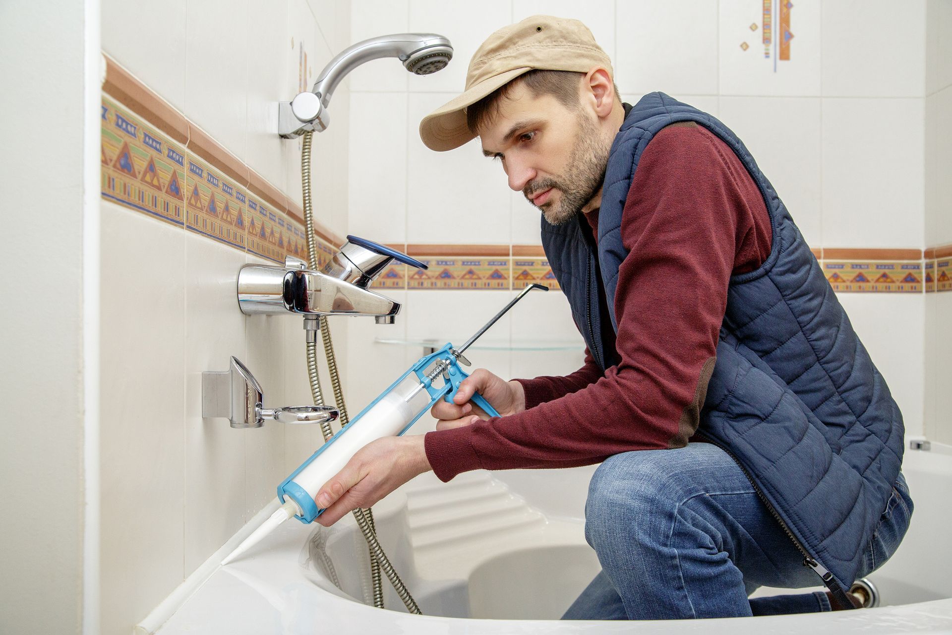 Plumber sealing a bathtub faucet with caulk in a tiled bathroom