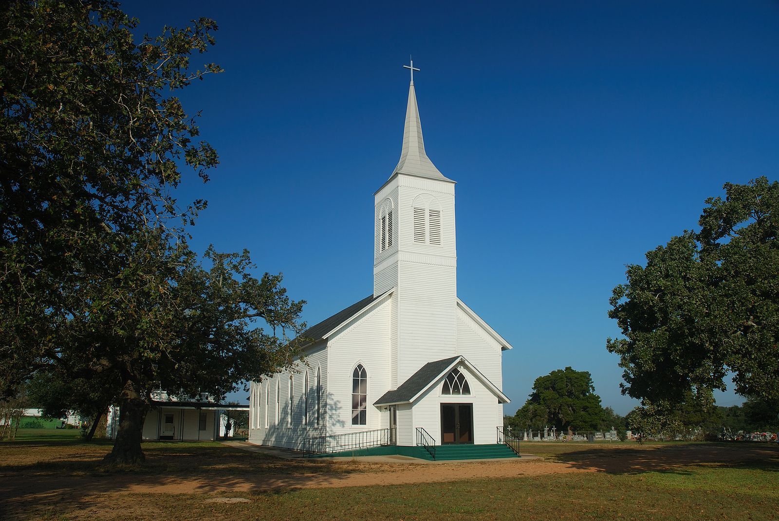 White church with tall steeple in a grassy field under a clear blue sky