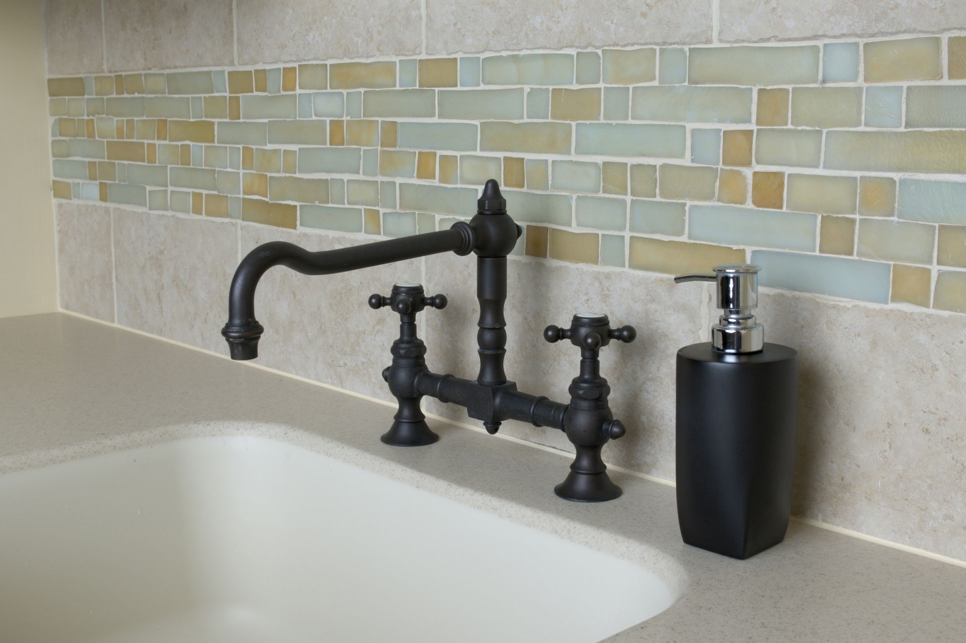 Black vintage bathtub faucet set on a bathroom counter beside a soap dispenser and tiled backsplash