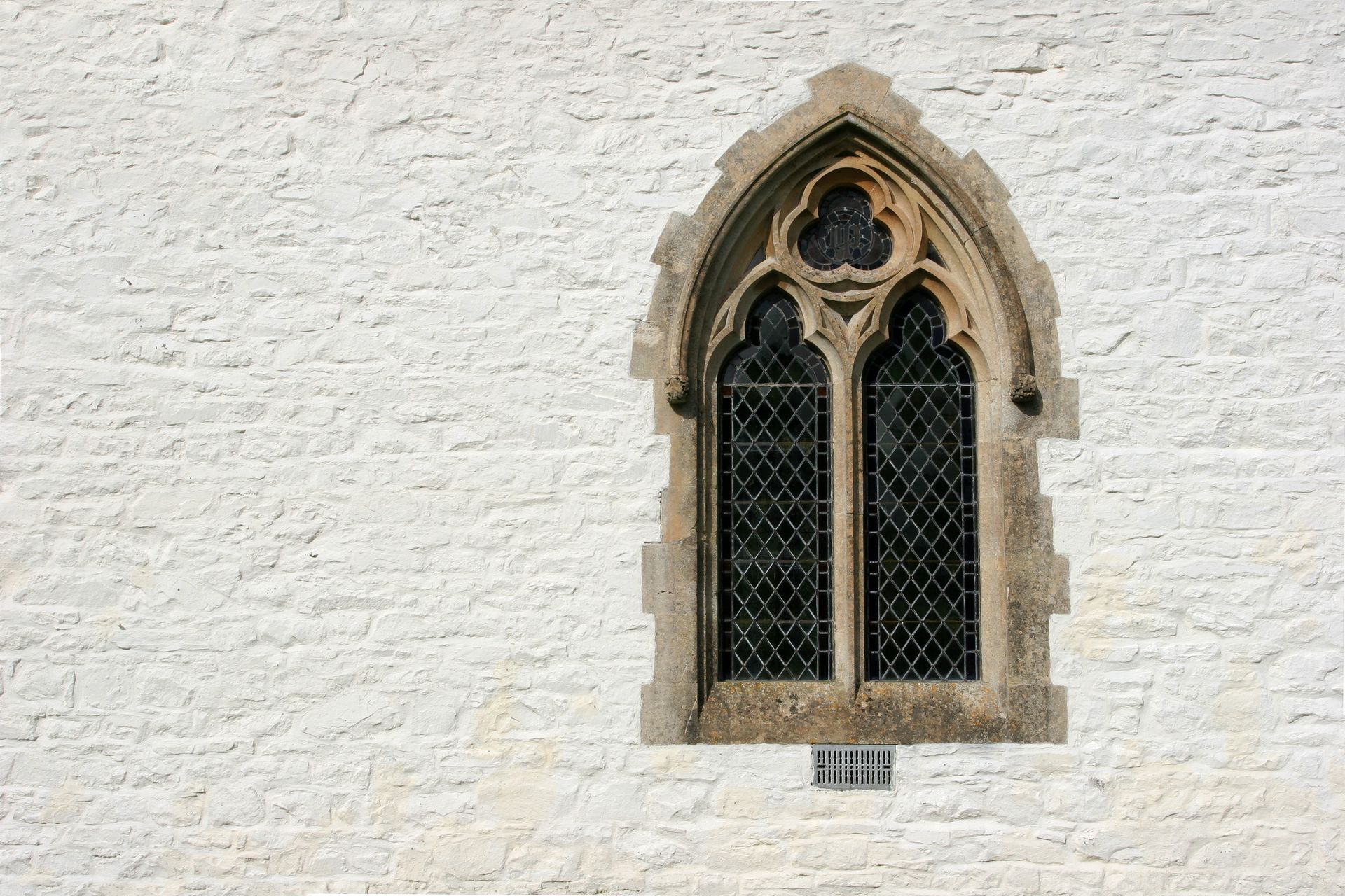 Small arched Gothic window with stone trim in a white stucco wall