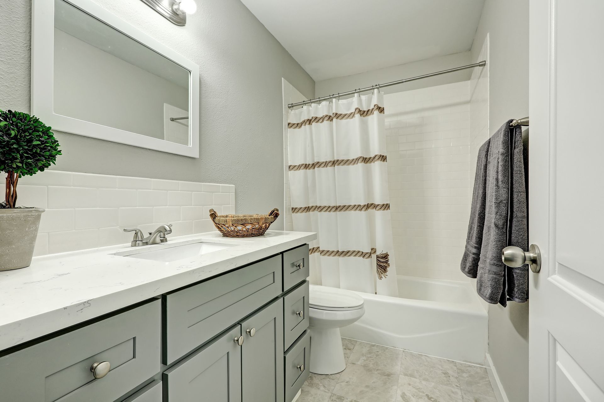 Bright modern bathroom with gray vanity, white tub, shower curtain, and wall mirror