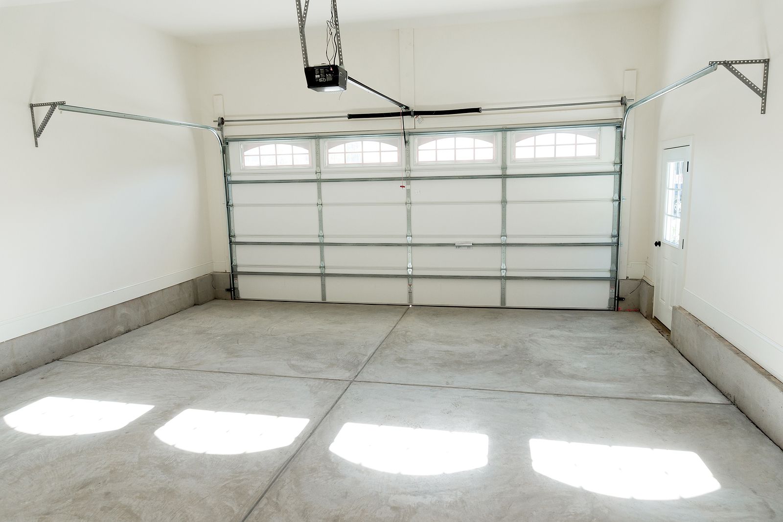 Empty garage with white walls, concrete floor, and a closed sectional garage door in bright daylight