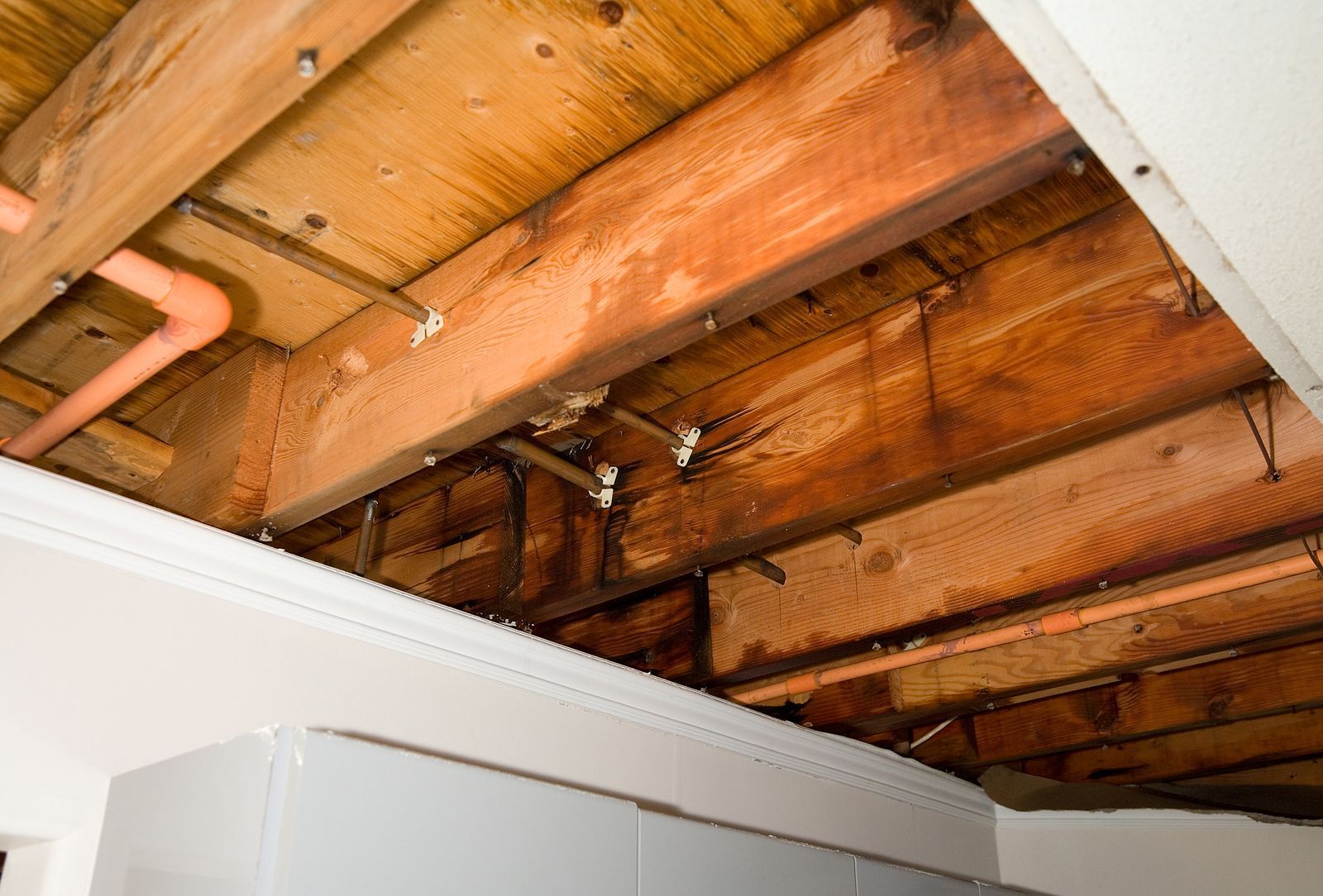 Exposed wooden ceiling joists with visible plumbing in an unfinished interior ceiling repair area
