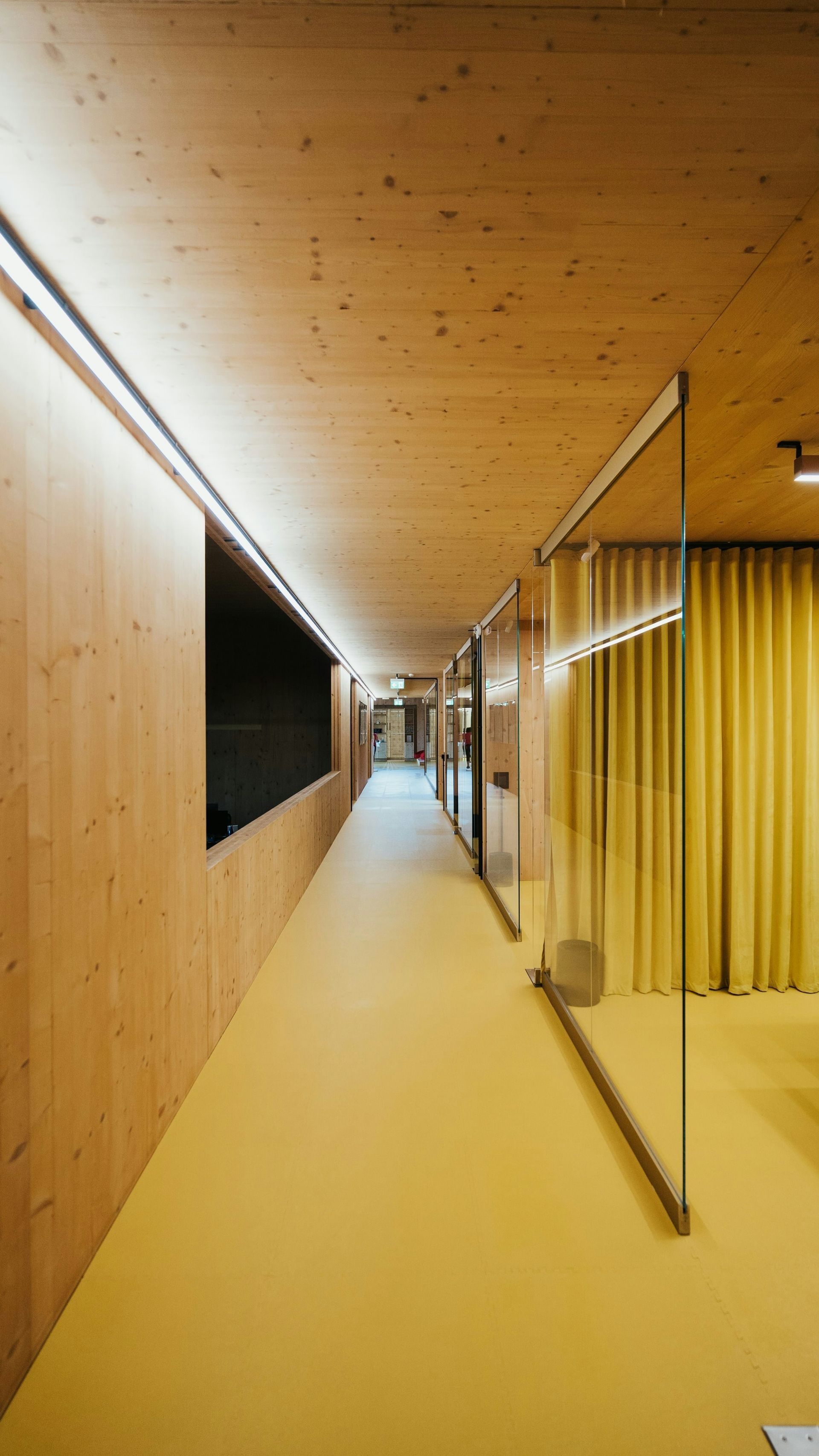 Minimalist hallway with wooden walls, a white floor, and a glass partition along the side.