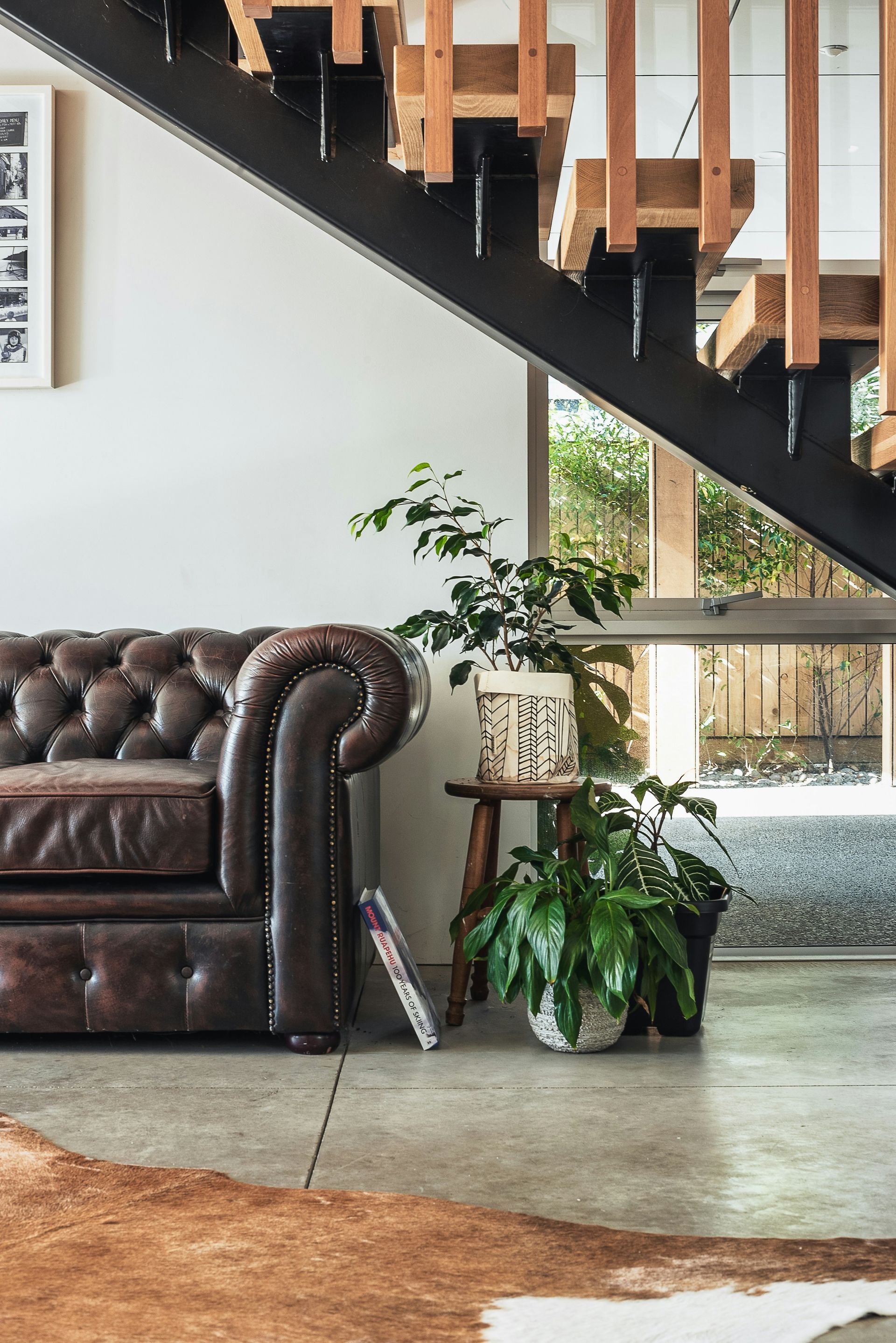 Living room with a brown leather sofa, potted plants, and a staircase with wooden railings
