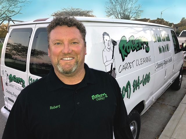 A man standing in front of a robert 's carpet cleaning van