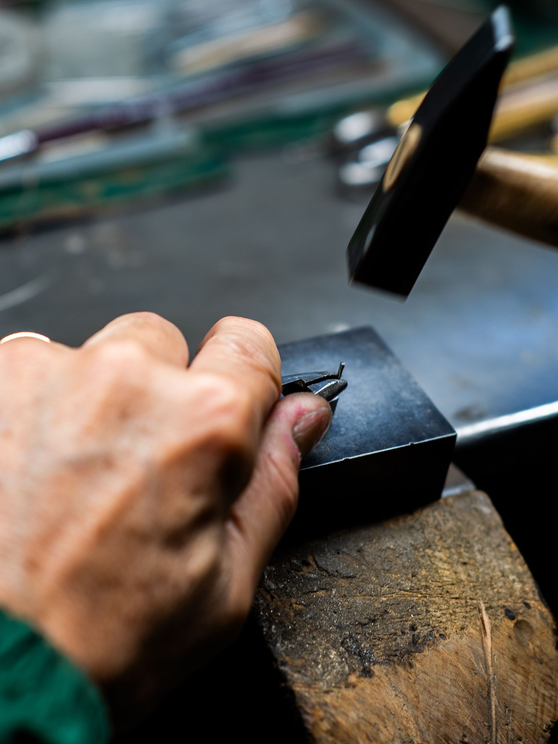 Una mano usa un piccolo martello per modellare un pezzo di metallo su un blocco su un banco da lavoro.