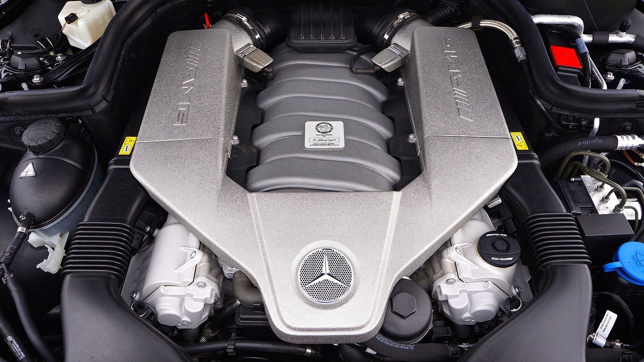 A high-angle view of a clean Maserati V8 car engine with a silver intake manifold and a centered trident emblem.