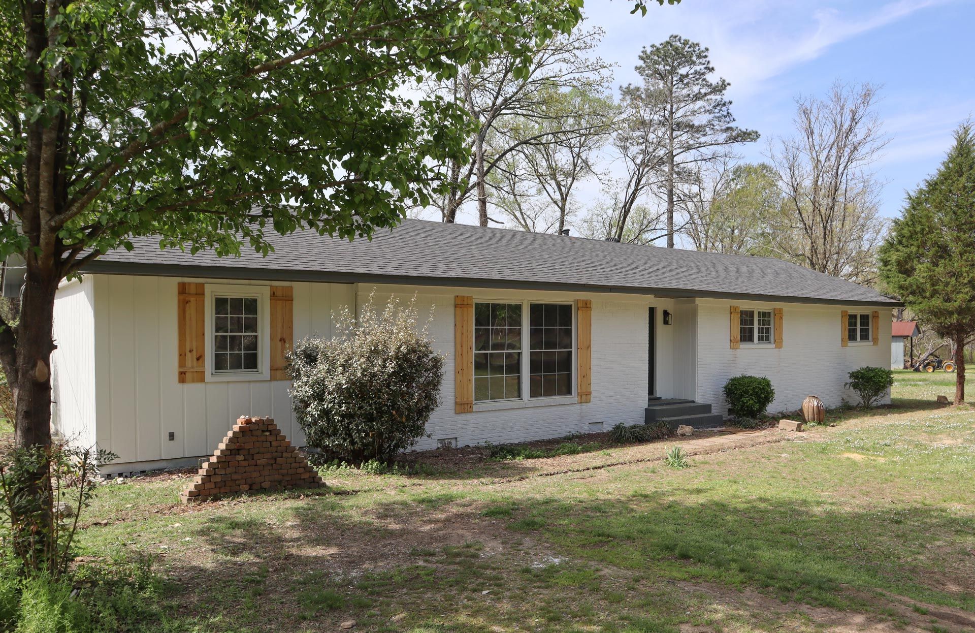 Single-story white house with yellow shutters, front yard trees, and a mailbox by the driveway