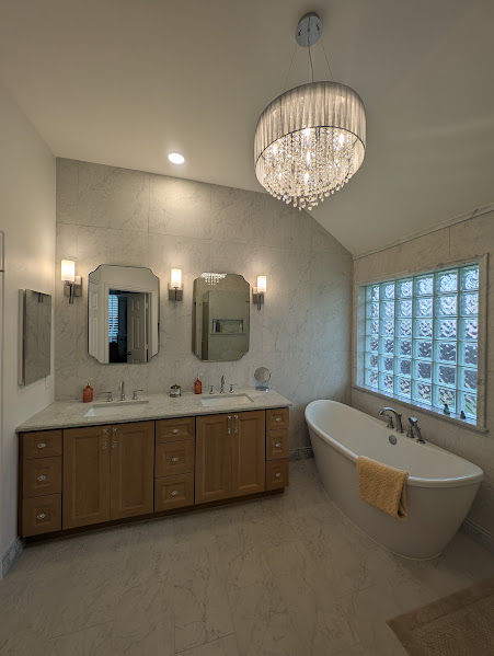 Elegant bathroom with chandelier, double vanity, and freestanding tub beside a glass-block window