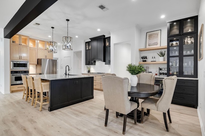 Modern open-concept kitchen and dining area with black island, light wood floors, and beige chairs