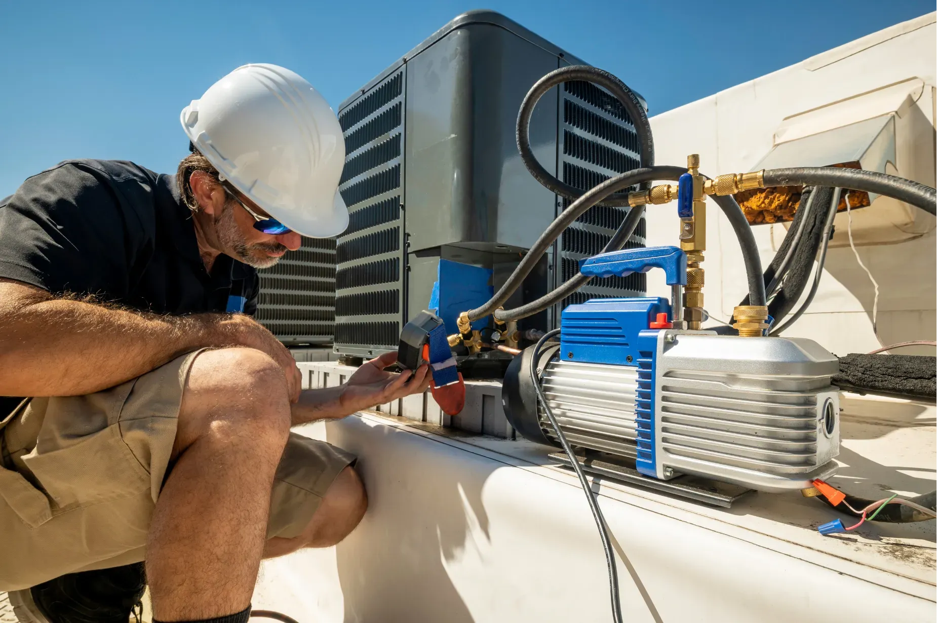 Worker in hard hat inspecting rooftop HVAC equipment with tools and cables