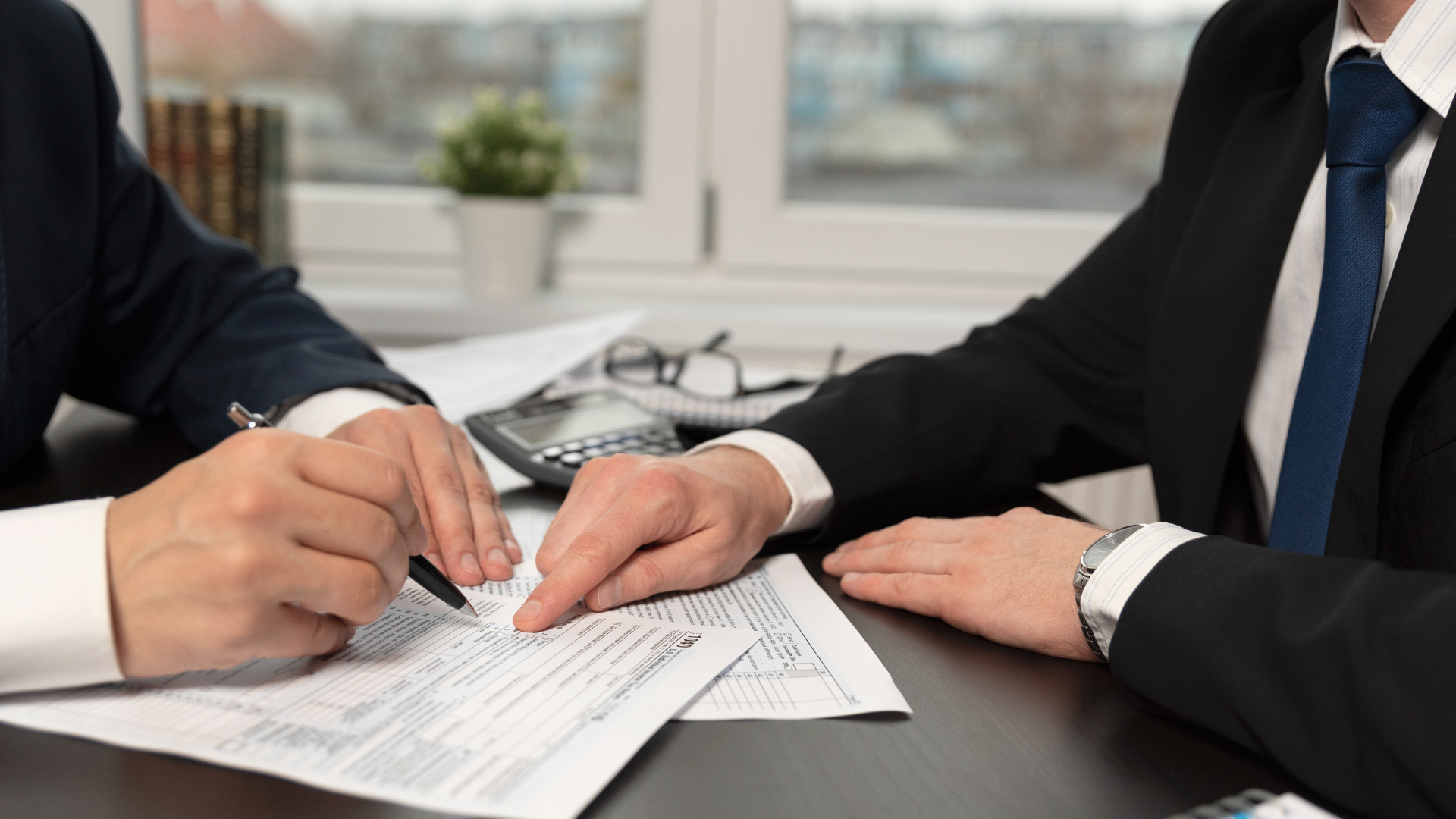 Two businesspeople signing a document at a desk in an office