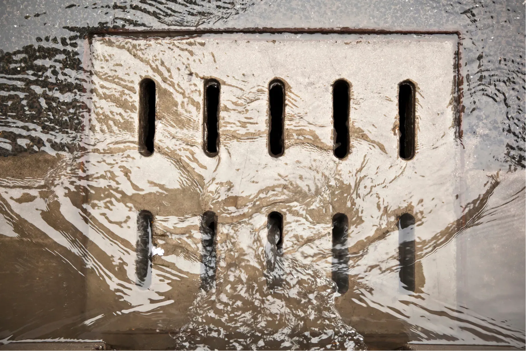 A beige vent grate with vertical slots, partially covered in muddy water or foam.