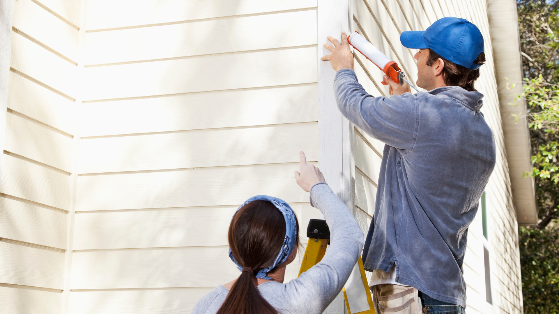 Two workers painting white house siding, one on a ladder and one below holding a brush