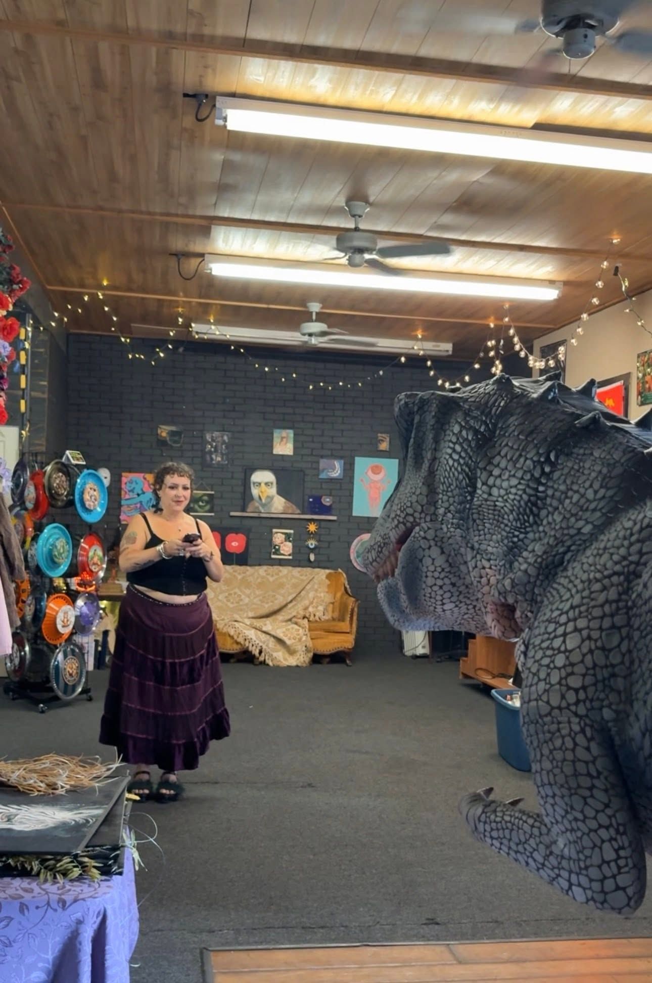 Woman in a purple dress stands in an art studio beside a large reptile sculpture.