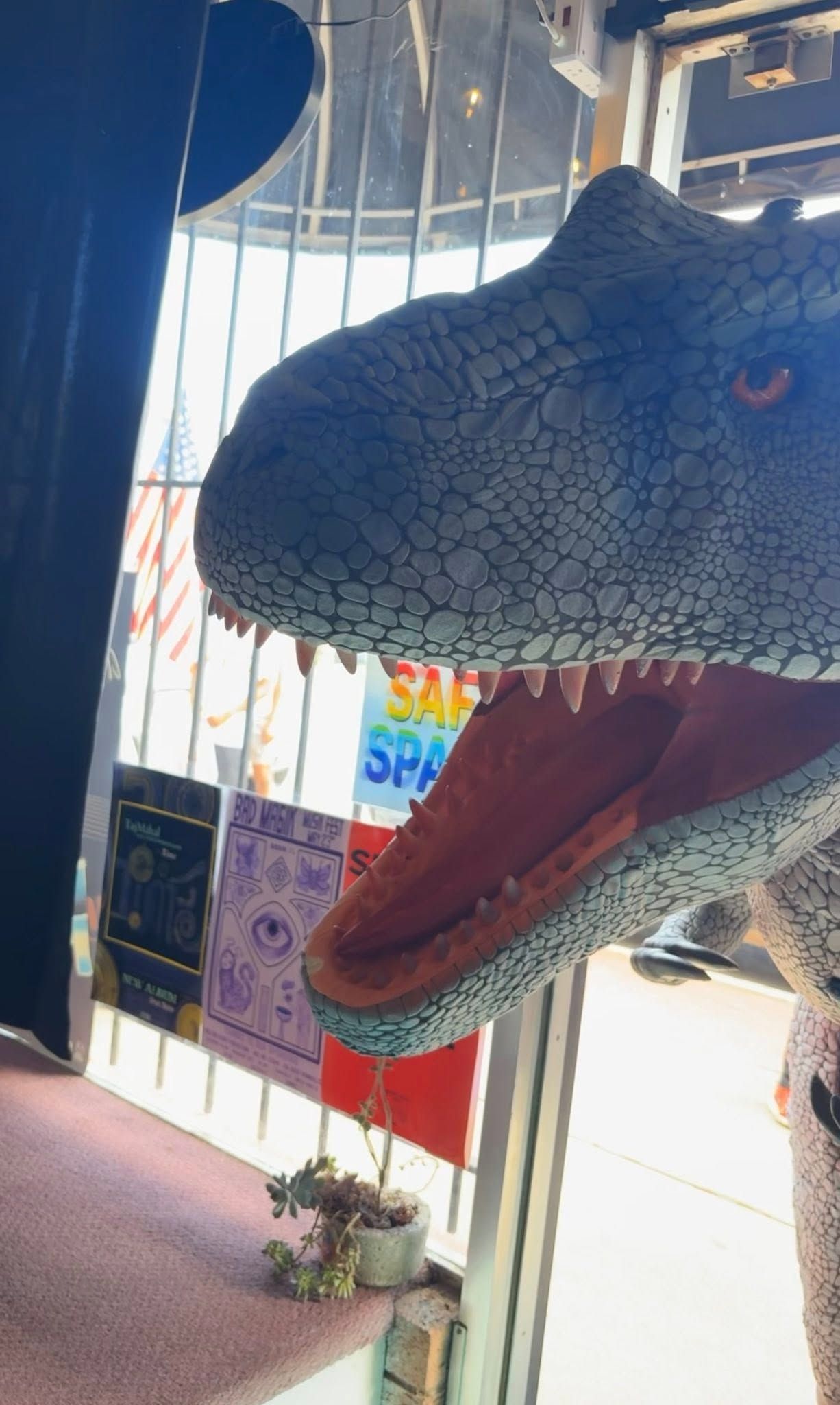 Close-up of a blue dinosaur statue with an open red mouth inside a bright indoor space