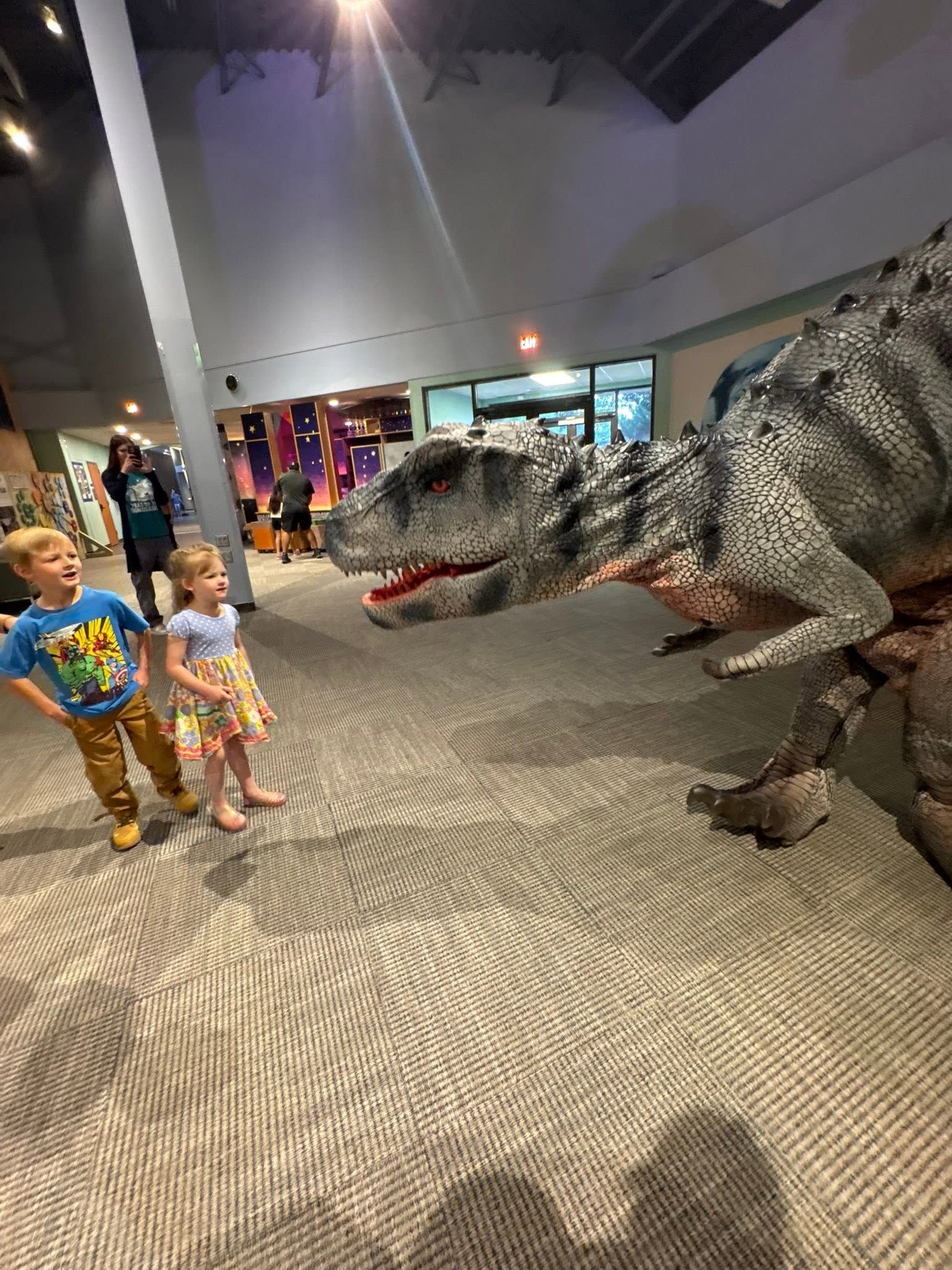 Children facing a life-sized T. rex exhibit in a museum lobby