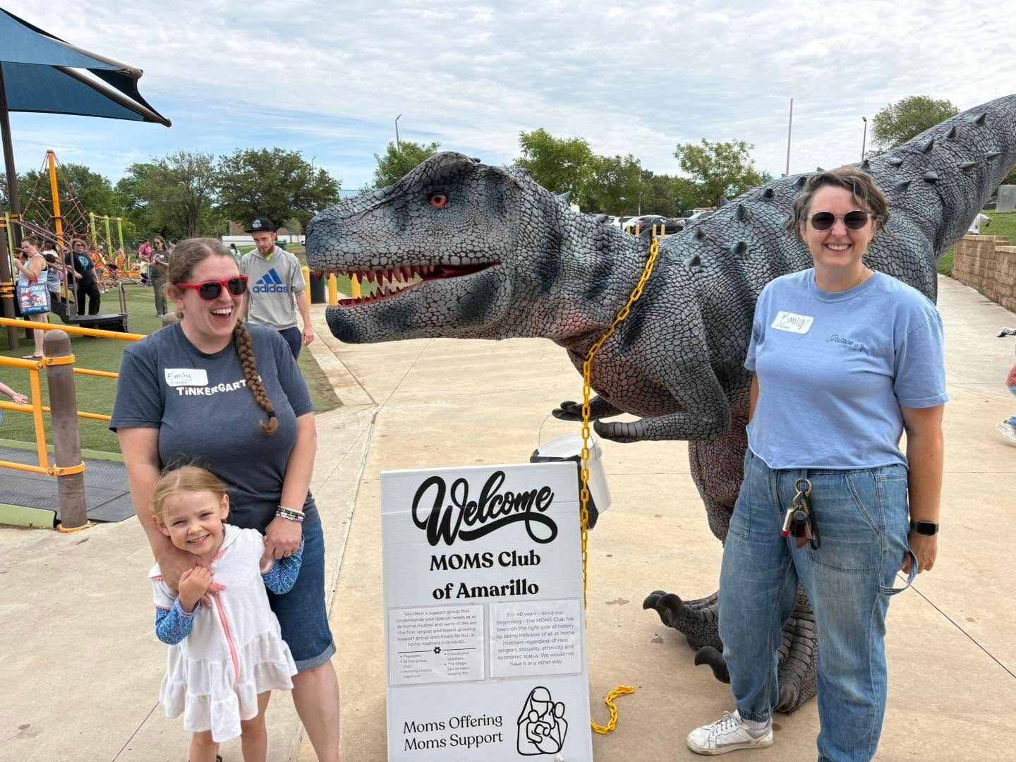 Family posing beside a dinosaur sculpture and welcome sign at a park entrance