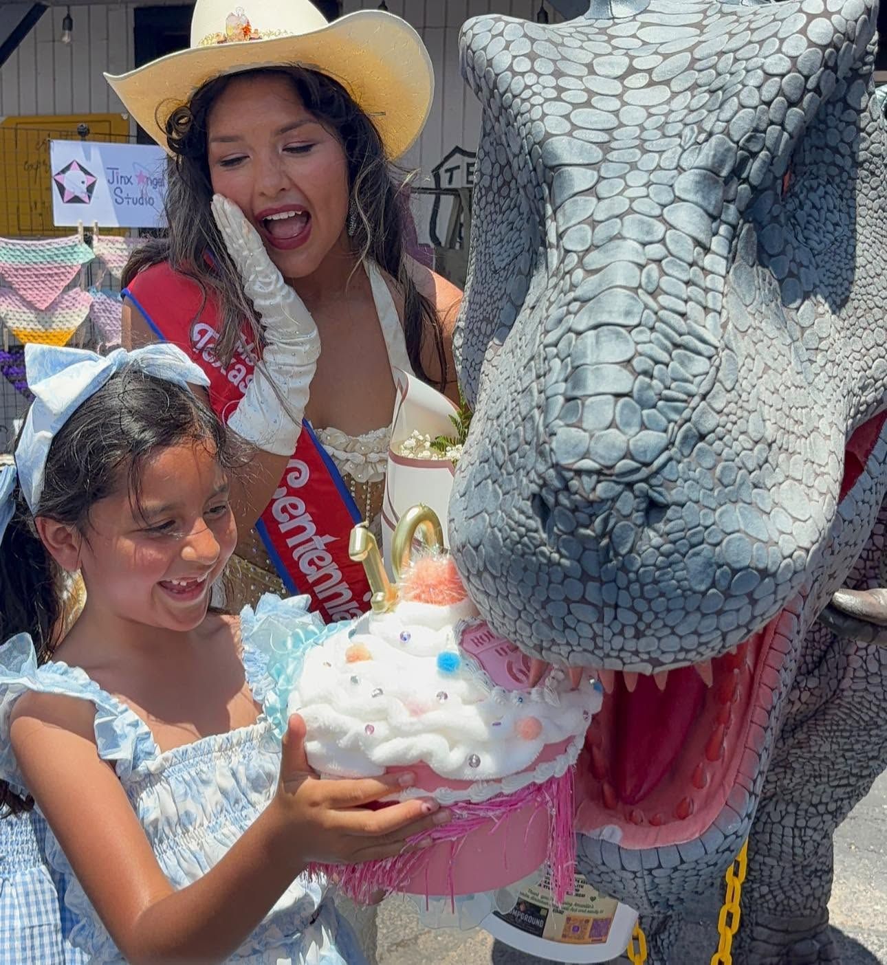 Girl holding a cupcake beside a large dragon head float at a colorful outdoor event