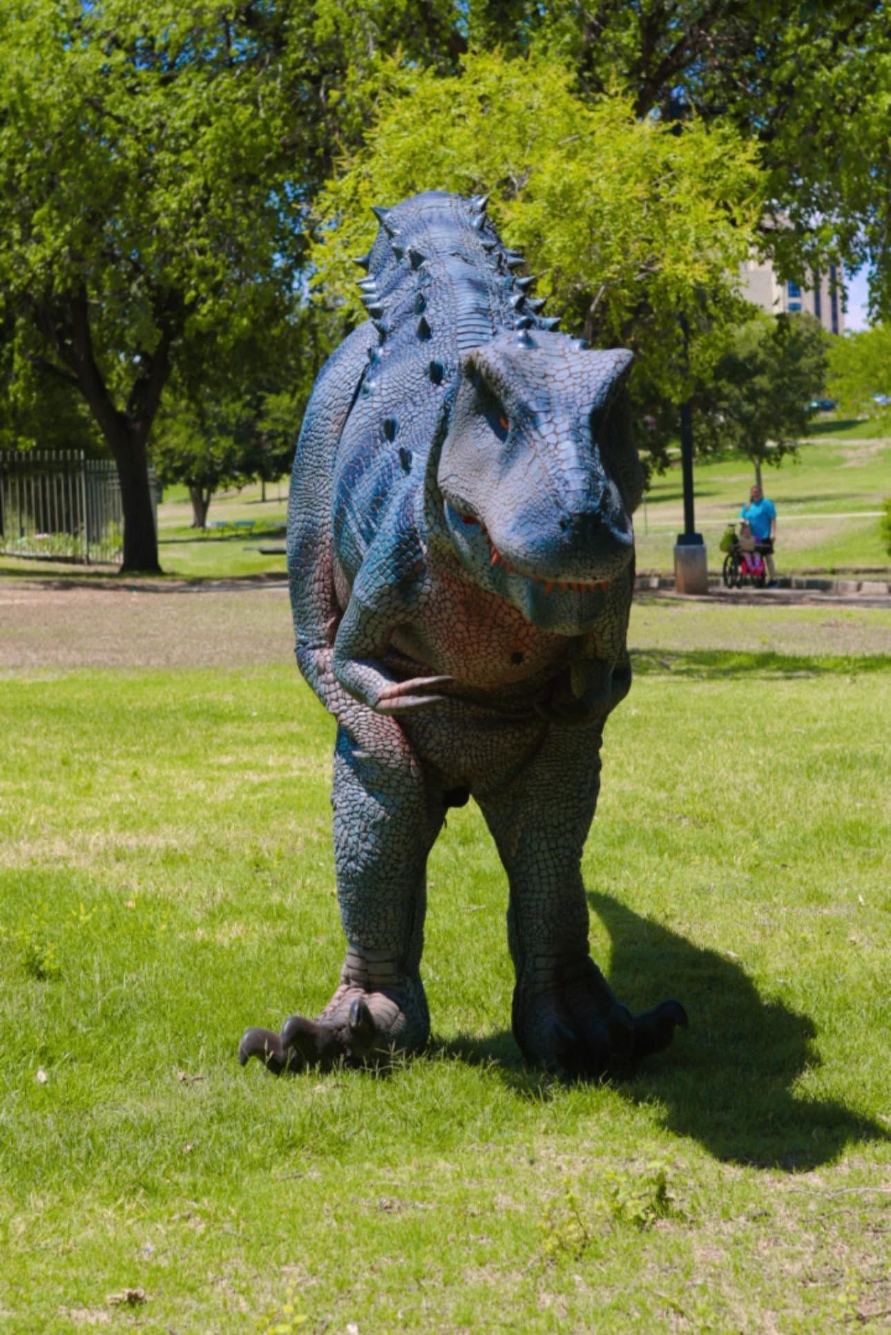 Blue dinosaur statue standing on grass in a sunny park
