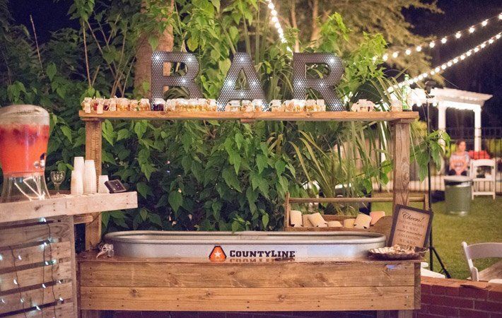 Outdoors bar setup with lit “F.A.R.” marquee letters and wooden counter under string lights