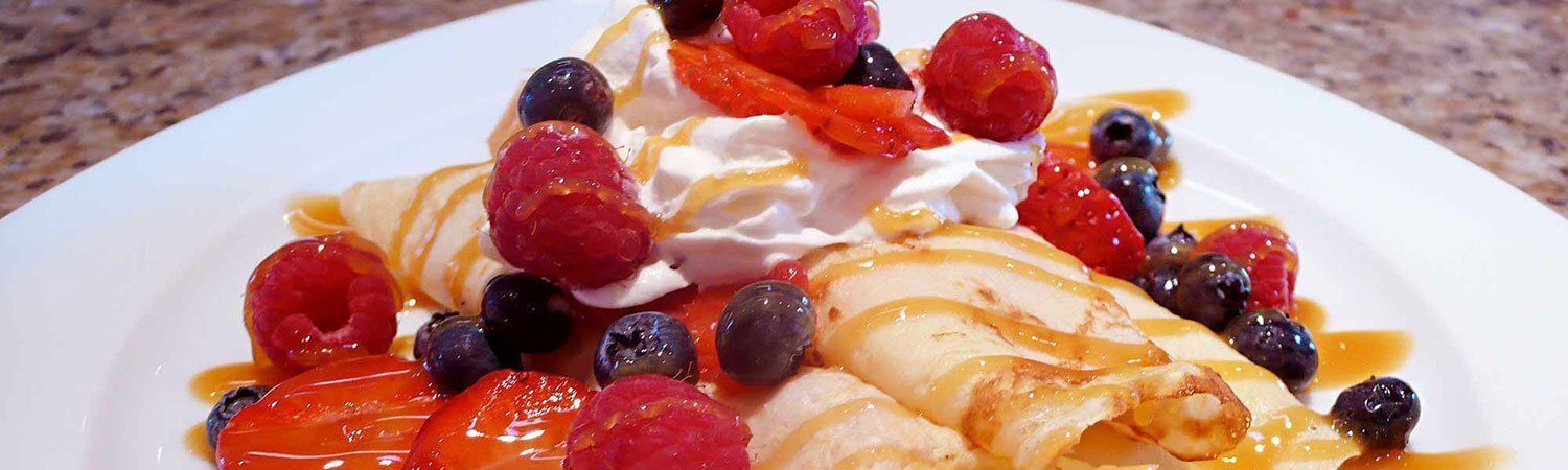 Pancakes topped with strawberries, blueberries, raspberries, and whipped cream on a white plate