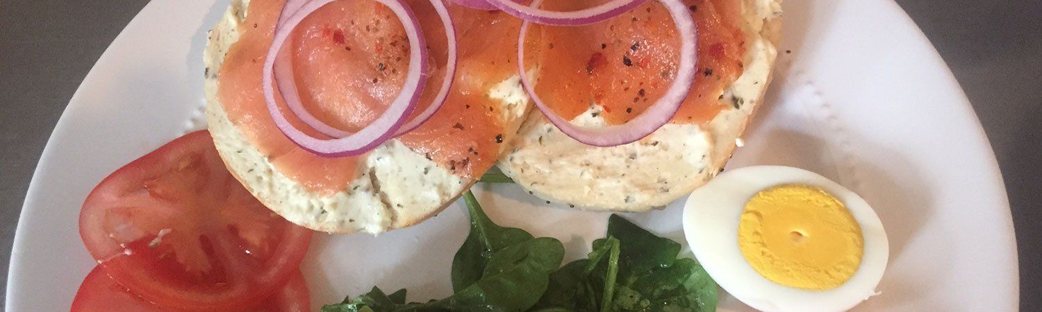 Plate with two bagel sandwiches, tomato slices, greens, and a halved boiled egg on a white plate