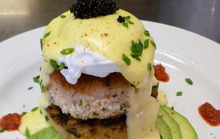 Stacked gourmet dessert with yellow topping, white cream, green garnish, and black caviar on a white plate