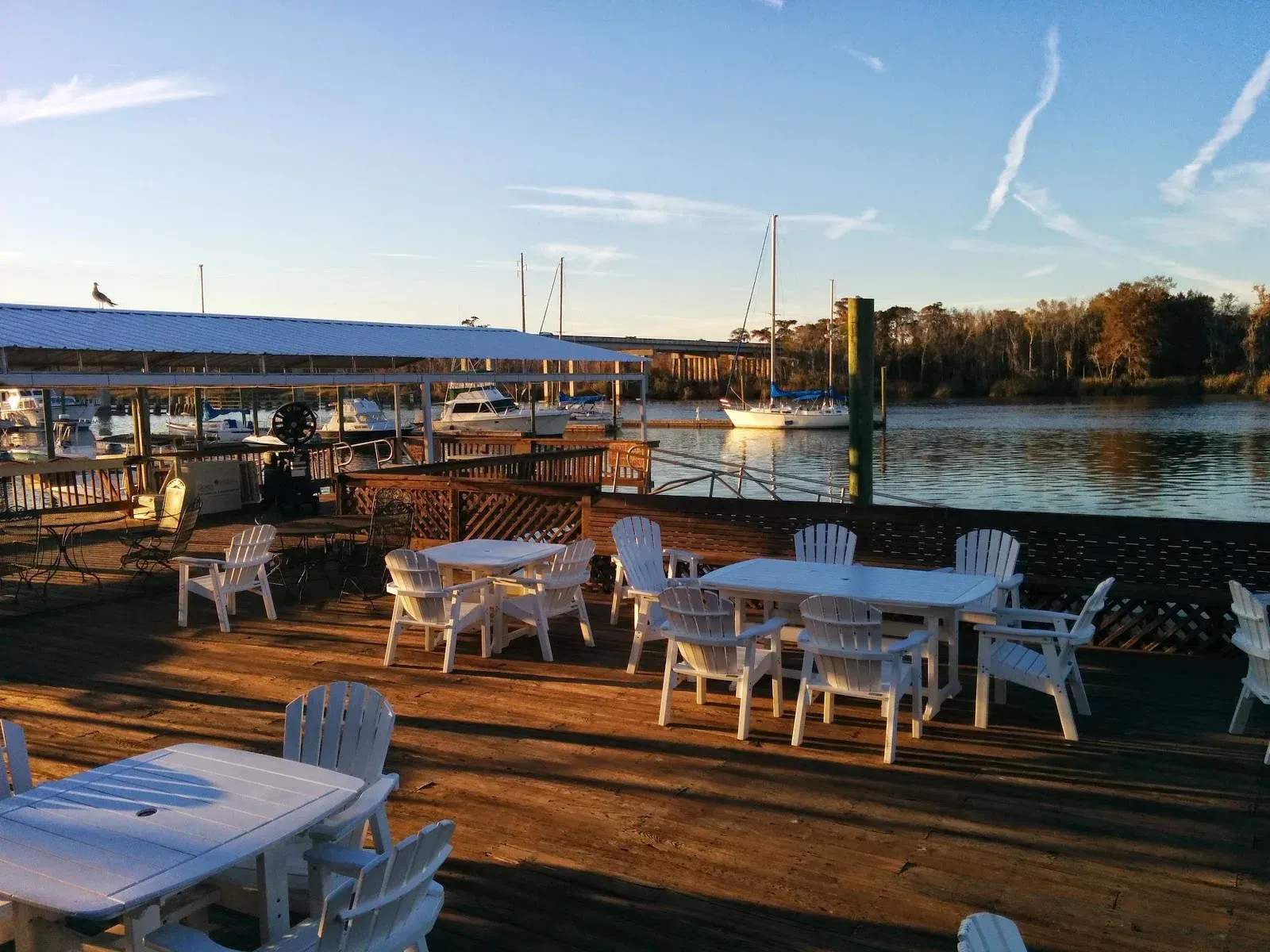 White patio tables on a wooden dock by a calm waterfront at sunset