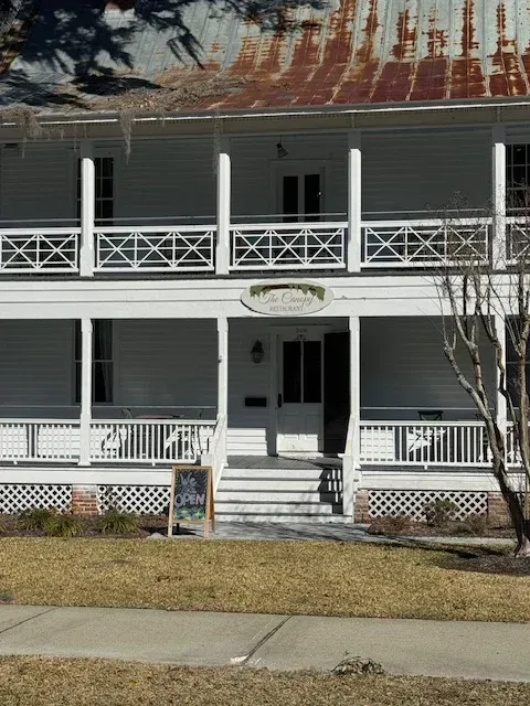 Two-story white porch house with a rusted metal roof and front steps by the sidewalk