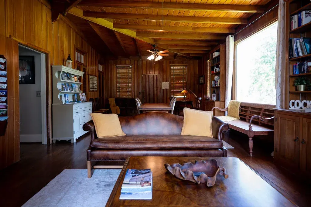 Rustic wooden lodge living room with benches, coffee table, and bookshelves by large windows